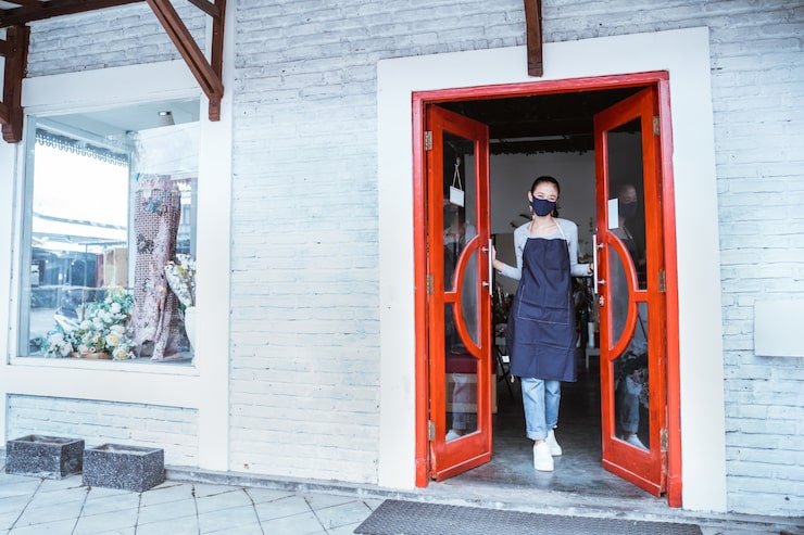 florist-woman-wearing-apron-face-mask-standing-open-door-flower-shop_8595-24407
